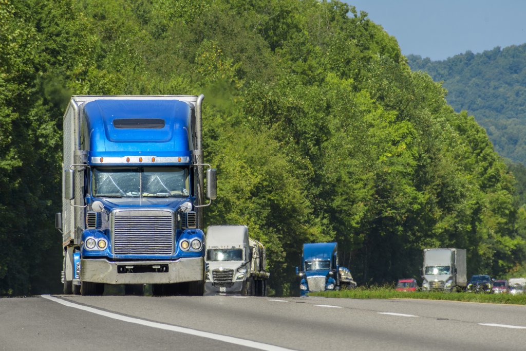 A blue semi leads a line of traffic down an Interstate in eastern Tennessee. Heat waves rising from the hot asphault creates a blurring effect on background trucks and foreground pavement.