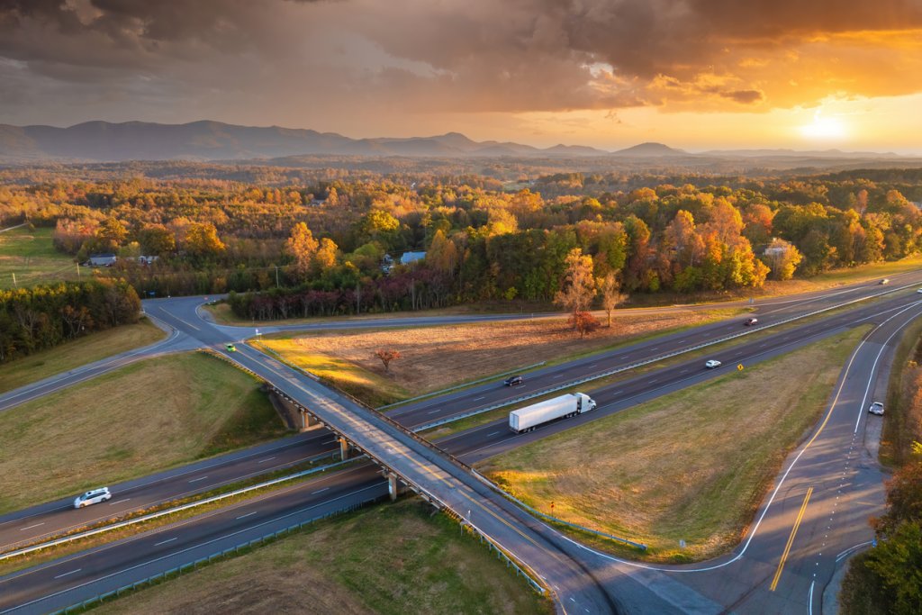 Freeway overpass junction with fast moving traffic cars and trucks in American rural area at sunset. Interstate transportation infrastructure in USA.