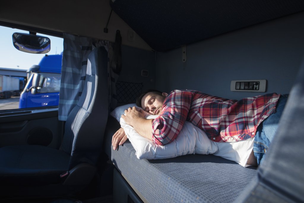 Truck driver sleeping in his cabin after working long routes overtime. Sleepy trucker taking a nap on a bed inside truck transporter. Lack of sleep.